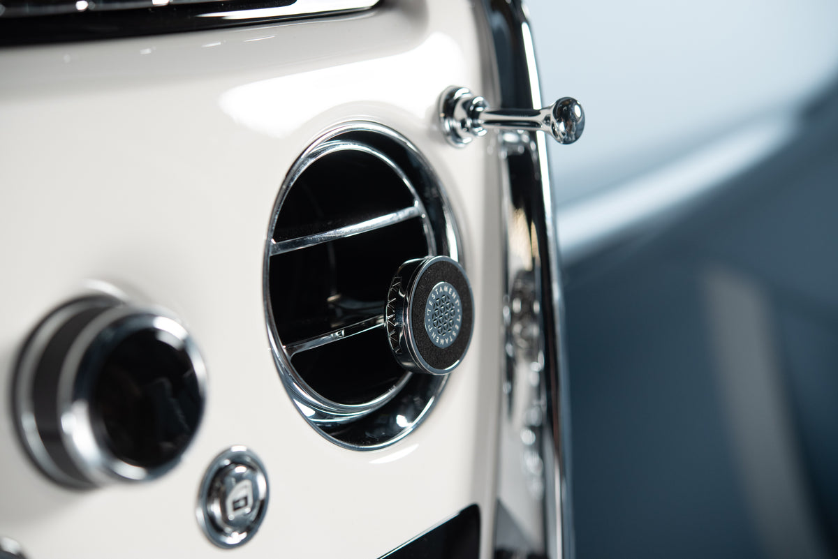 Close-up of a vintage car's cream-colored front grille and chrome air vents, featuring a circular black and chrome air dam on the right side.